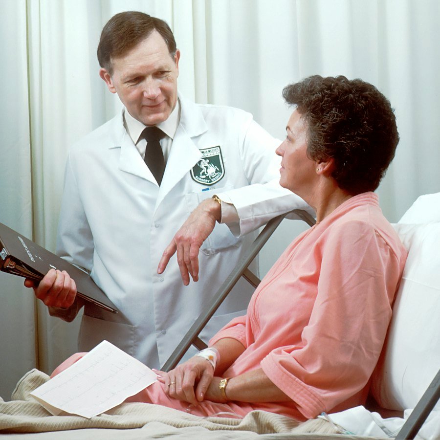 A doctor in a white coat speaking with a patient sitting up in a hospital bed
