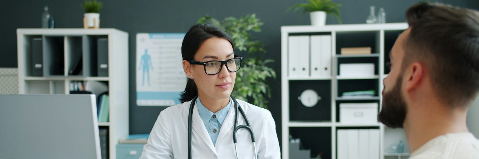 A clinician in a white coat reviewing paperwork with a patient at a desk